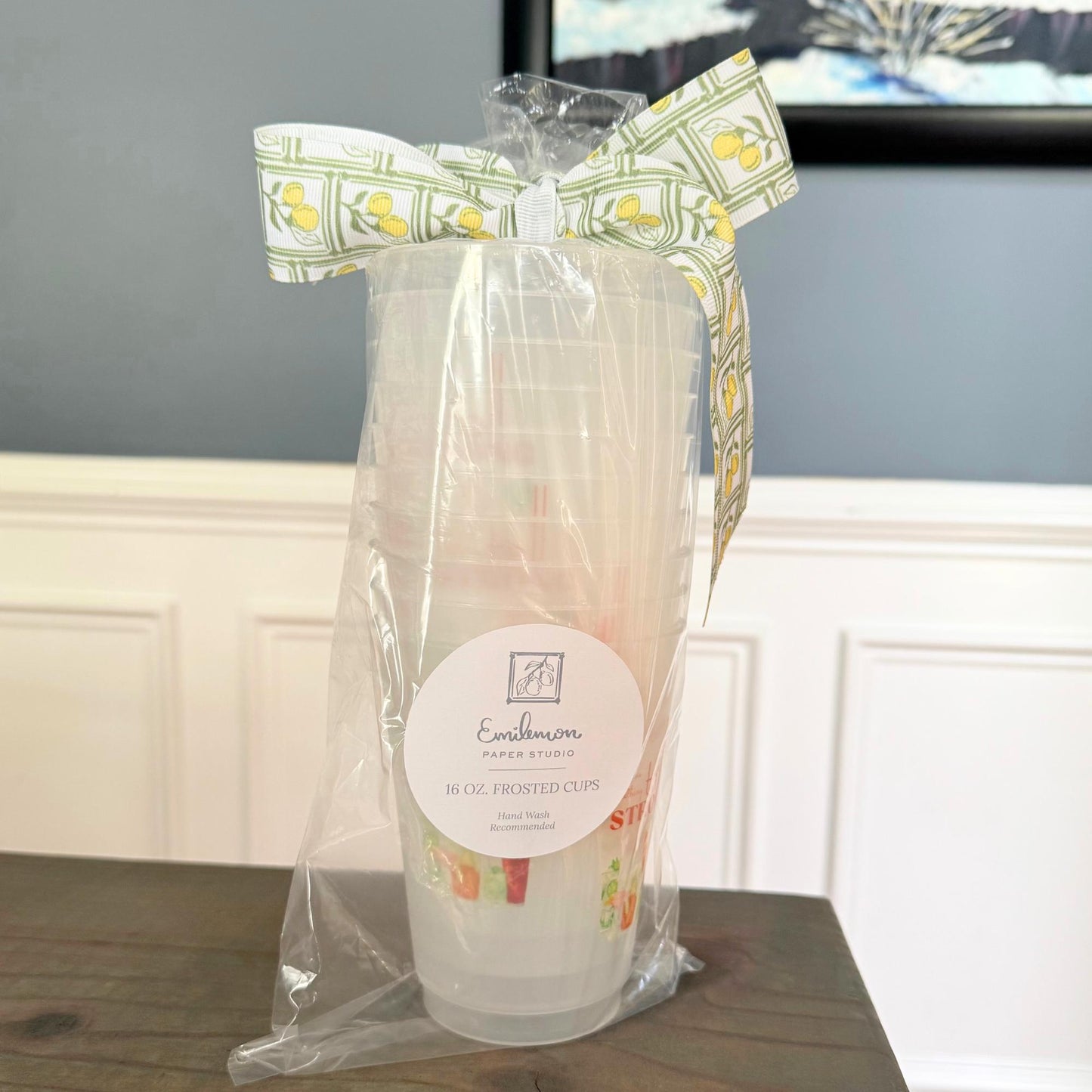 A clear plastic cup with a yellow and green pattern, tied with a yellow and green ribbon, and labeled as "Emilion Paper Cups" in the center of the image.