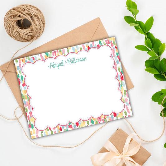 a personalized note card with a scalloped edge, a gift box, a spool of twine, and some greenery.