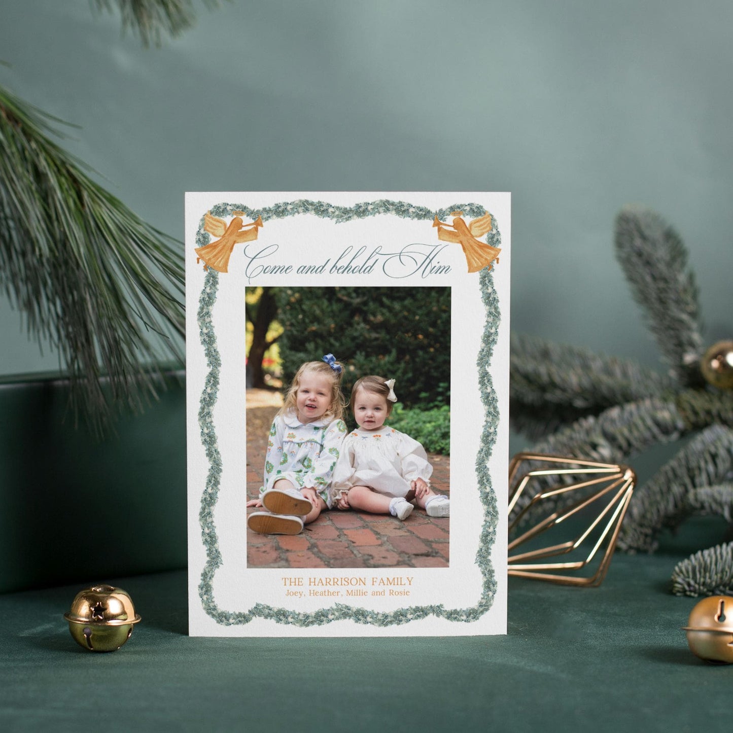 a white card with a photo of two young girls sitting on a brick path, surrounded by Christmas decorations and ornaments.