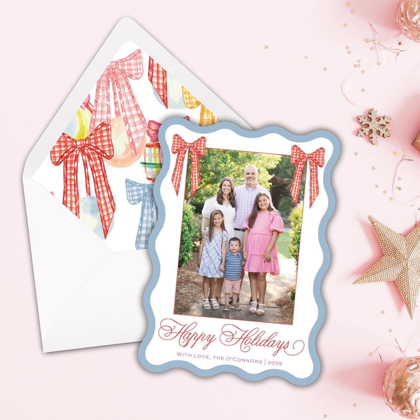 A family portrait of a group of people, including adults and children, is displayed in a frame with a holiday greeting. The frame is placed on a pink background, and there are Christmas decorations and ornaments around it.