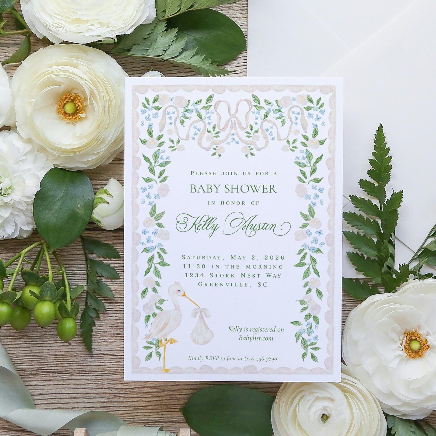 The image is a baby shower invitation featuring a floral design with white flowers and green leaves.