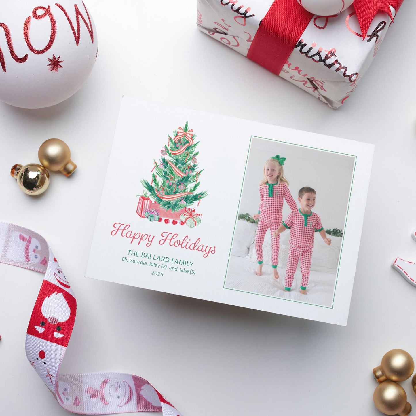 A holiday card featuring two children in red and white checkered pajamas, with a Christmas tree and presents, surrounded by ornaments and a gift box.