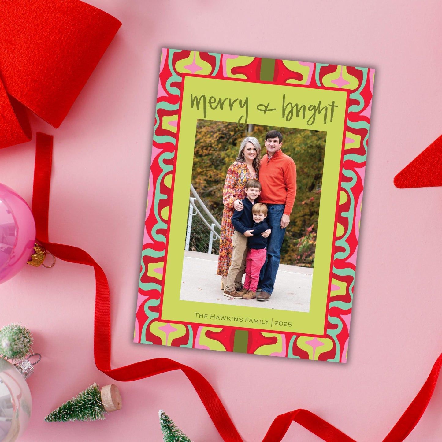 A colorful holiday greeting card featuring a family photo, surrounded by festive decorations such as a red ribbon, a small Christmas tree, and other holiday ornaments.