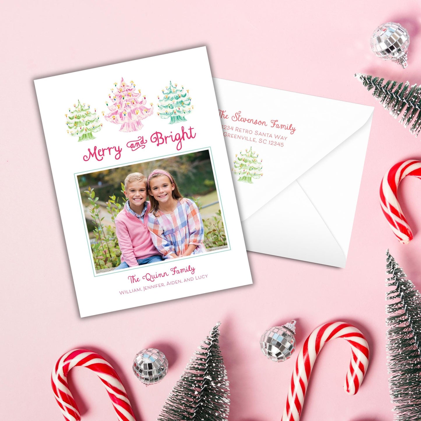 A Christmas card with a photo of two children, surrounded by candy canes, ornaments, and a Santa Claus tree on a pink background.