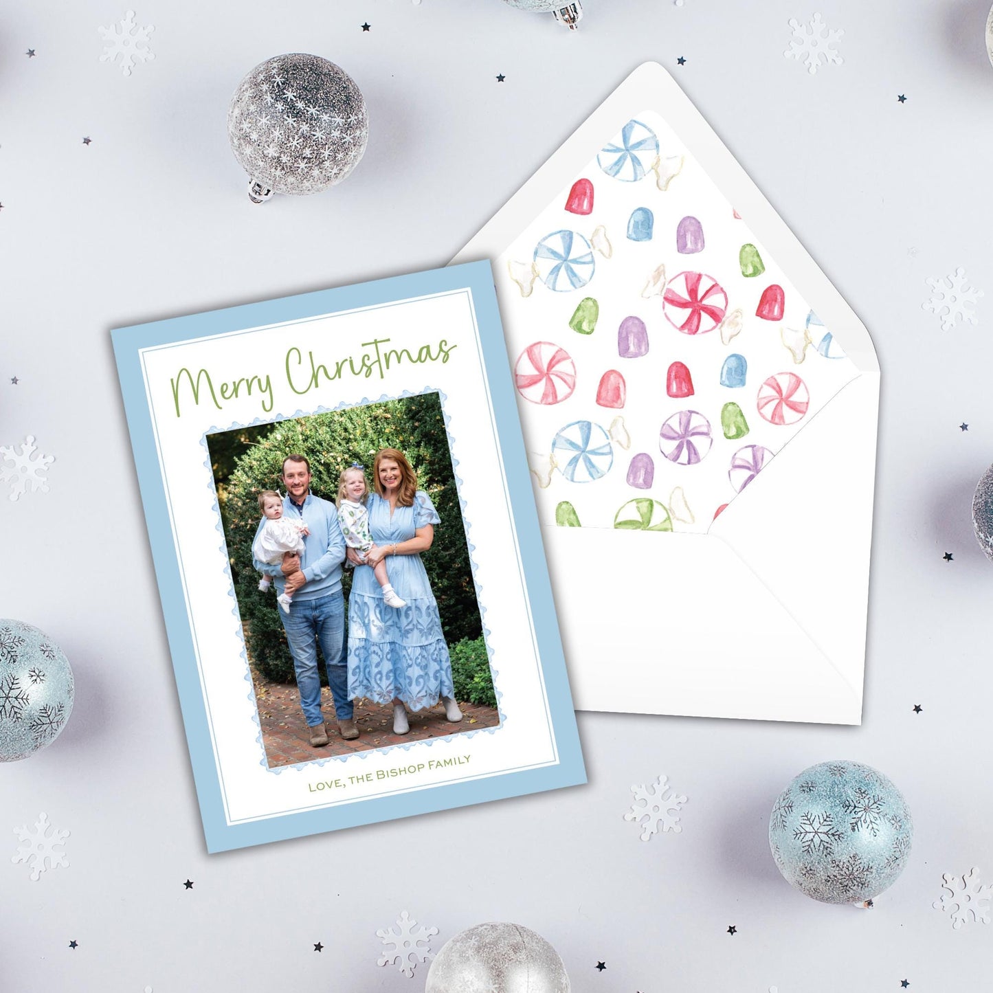 A Christmas card with a family photo and a matching envelope, surrounded by ornaments and snowflakes on a white background.