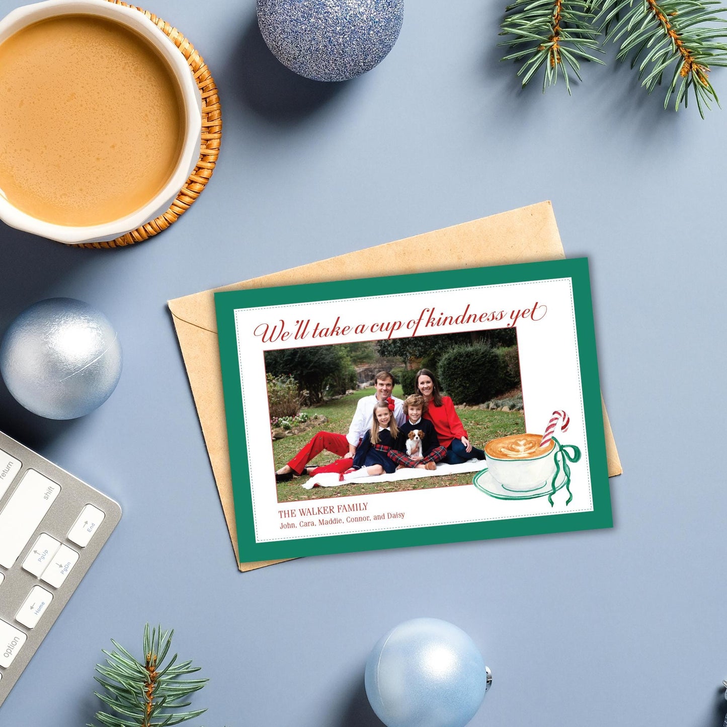 A Christmas card with a family photo and a message about taking a cup of kindness, along with some ornaments and a mug of coffee.