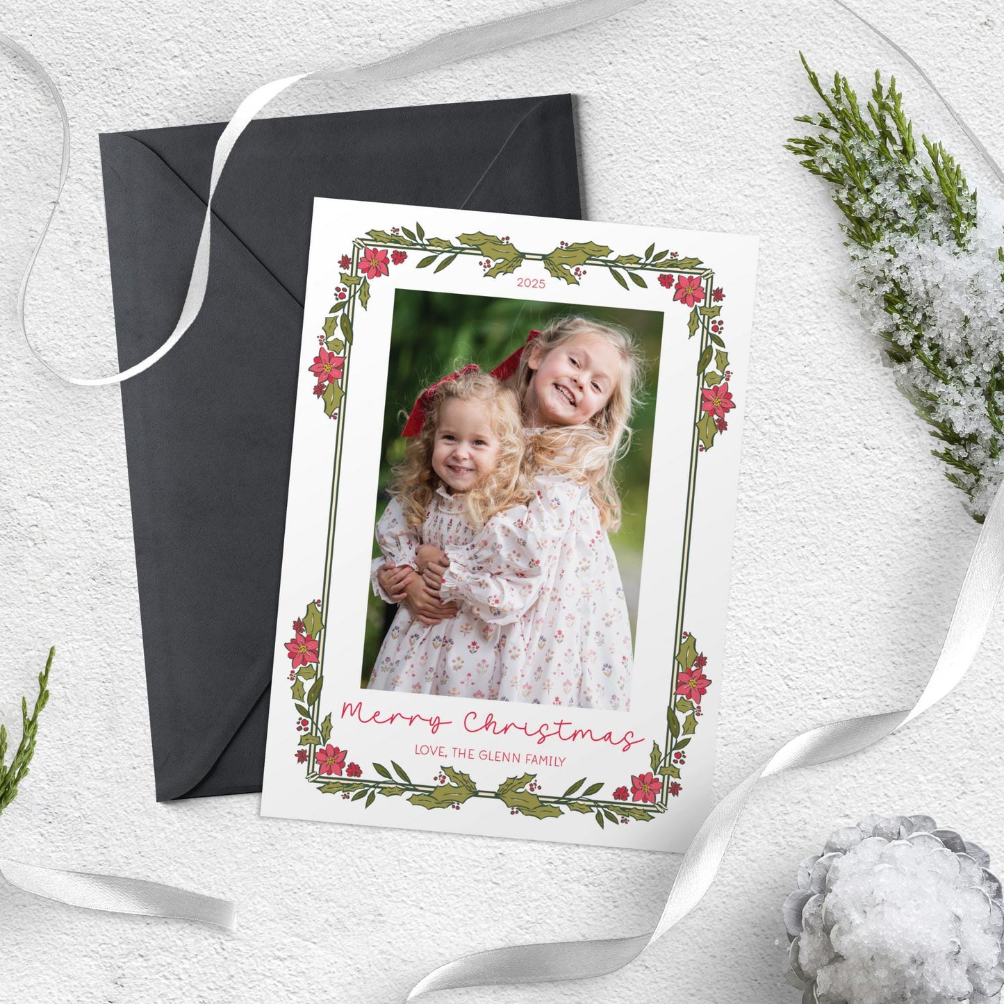 A Christmas card with a photo of two young girls, surrounded by holiday decorations such as a ribbon, pine branches, and snowflakes.