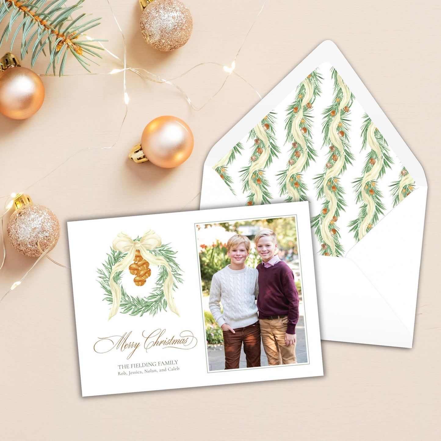 A Christmas card with a photo of two children, along with a wreath and ornaments, and an envelope with a patterned design.