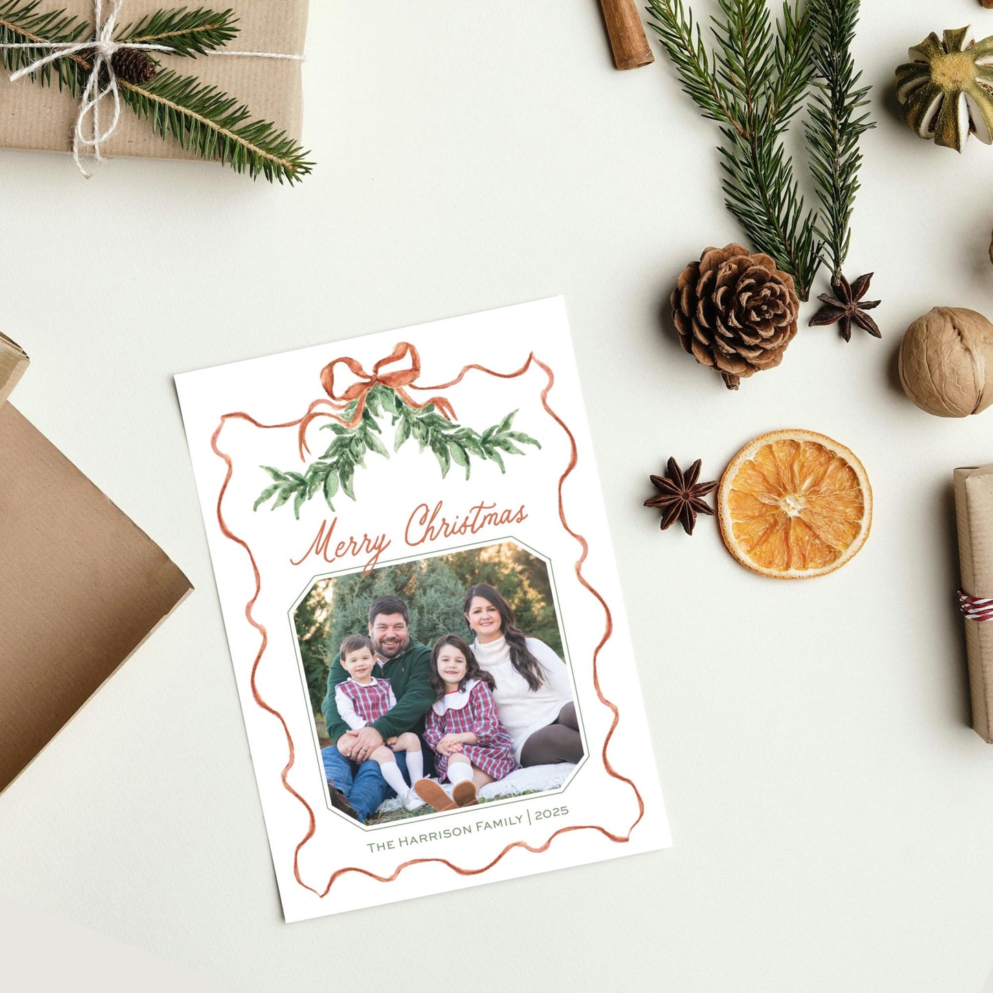 A white card with a photo of a family, surrounded by Christmas decorations such as pine branches, pine cones, and an orange slice.