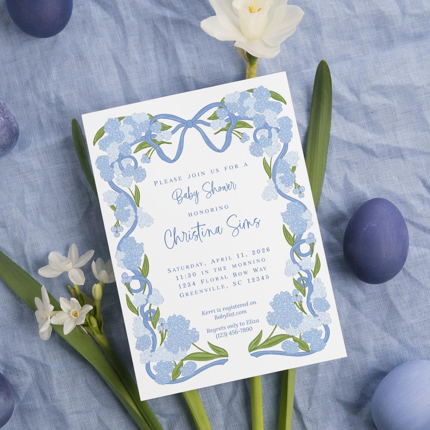 The image is a baby shower invitation featuring blue flowers and Easter eggs, with a blue and white color scheme.