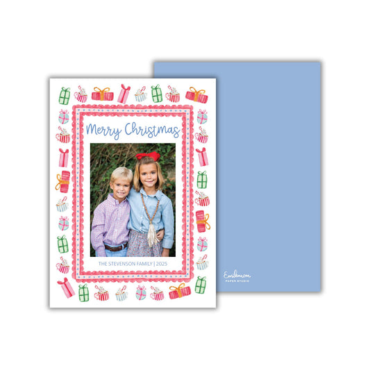 A Christmas card featuring two children, likely siblings, posing for a photo. The card has a festive design with various Christmas-themed elements such as presents, trees, and other holiday decorations.