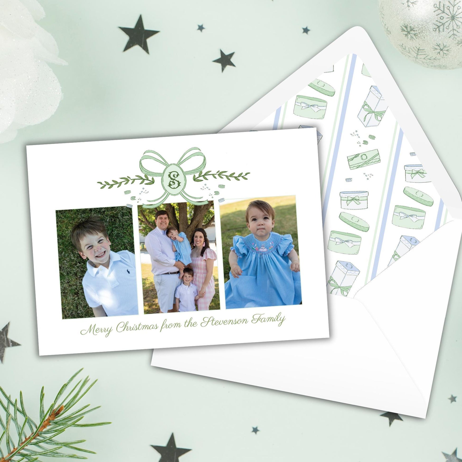 A family photo is displayed on a white card with a green ribbon, accompanied by a matching envelope with a pattern of Christmas-themed illustrations.