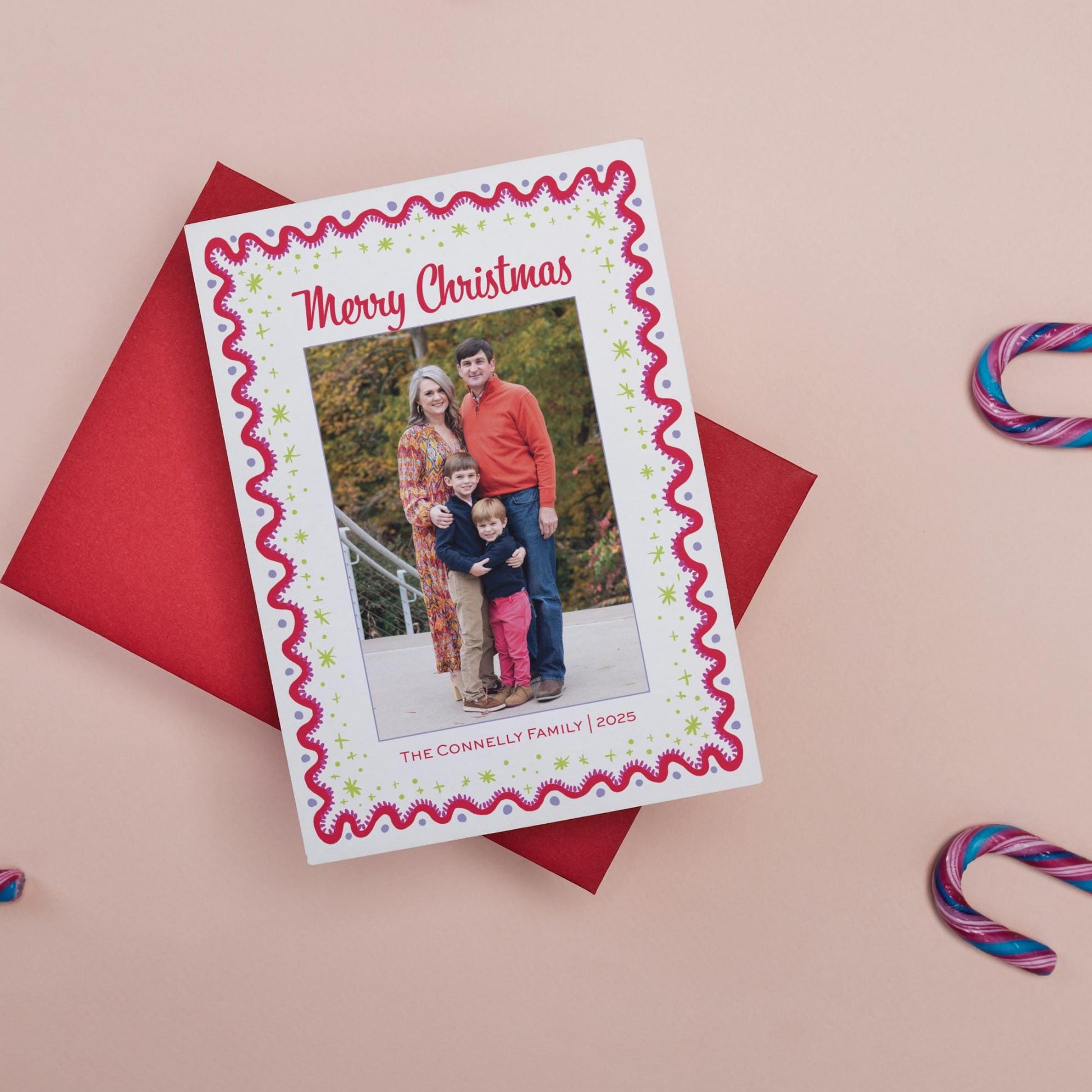 A family portrait of a man, woman, and child is displayed on a red card with a festive border, placed on a pink background with candy canes.