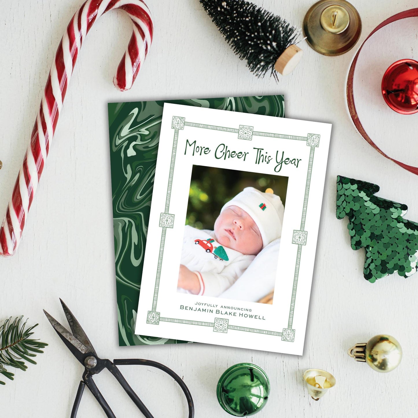 a Christmas card with a photo of a baby, surrounded by holiday decorations such as a candy cane, ornaments, and a small Christmas tree.