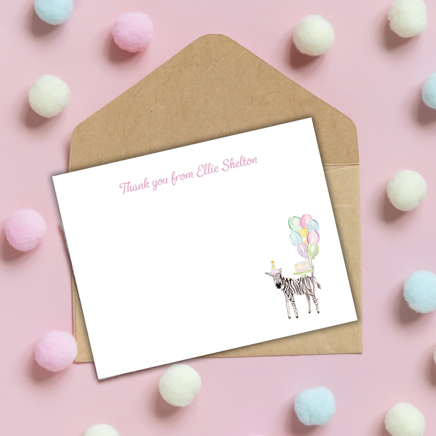 a blank card with a zebra illustration and a message, placed on a pink background with pom-poms scattered around.