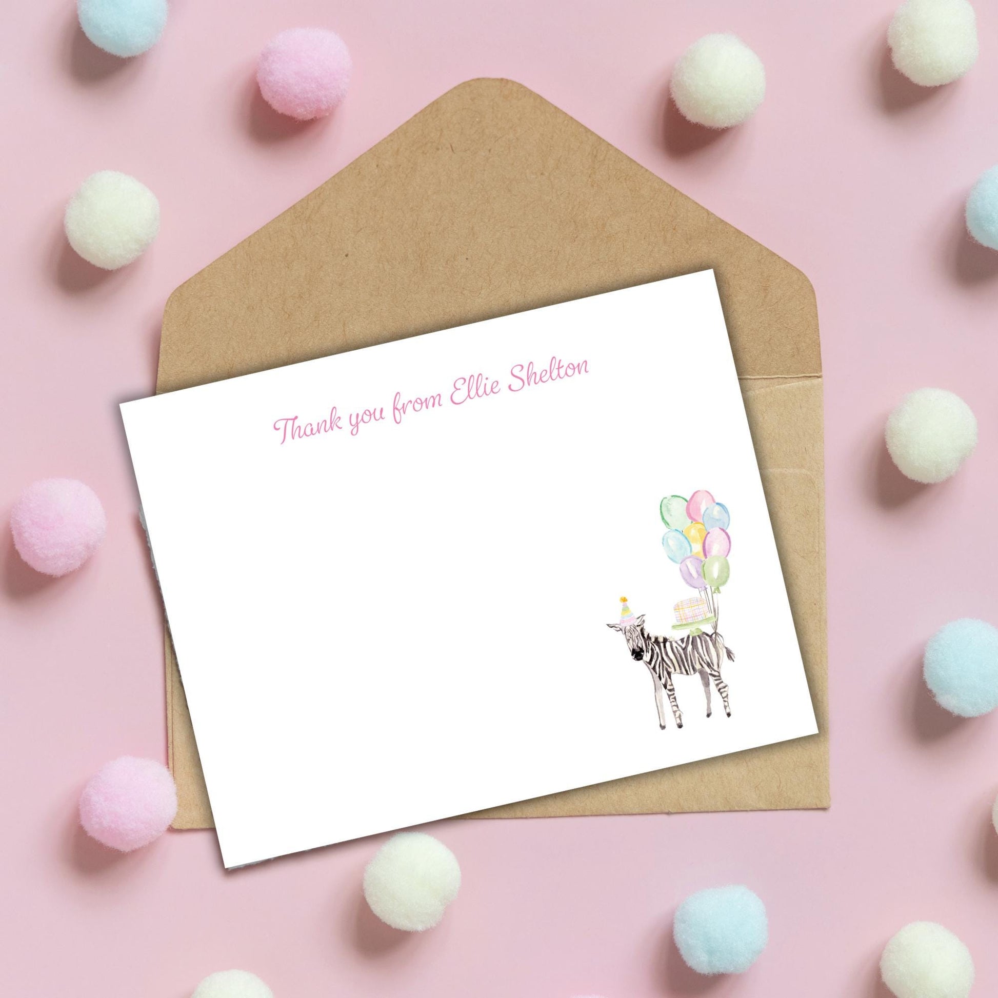 a blank card with a zebra illustration and a message, placed on a pink background with pom-poms scattered around.