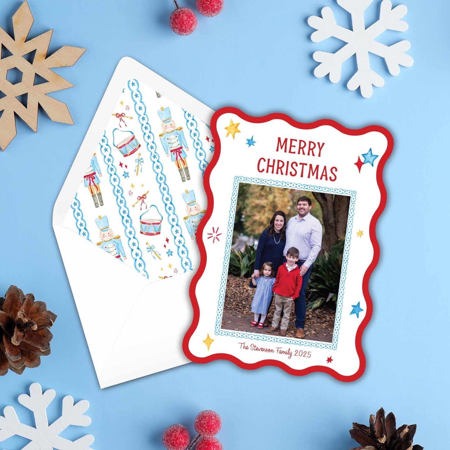 A Christmas card with a photo of a family is placed on a blue background, surrounded by snowflakes and pine cones.