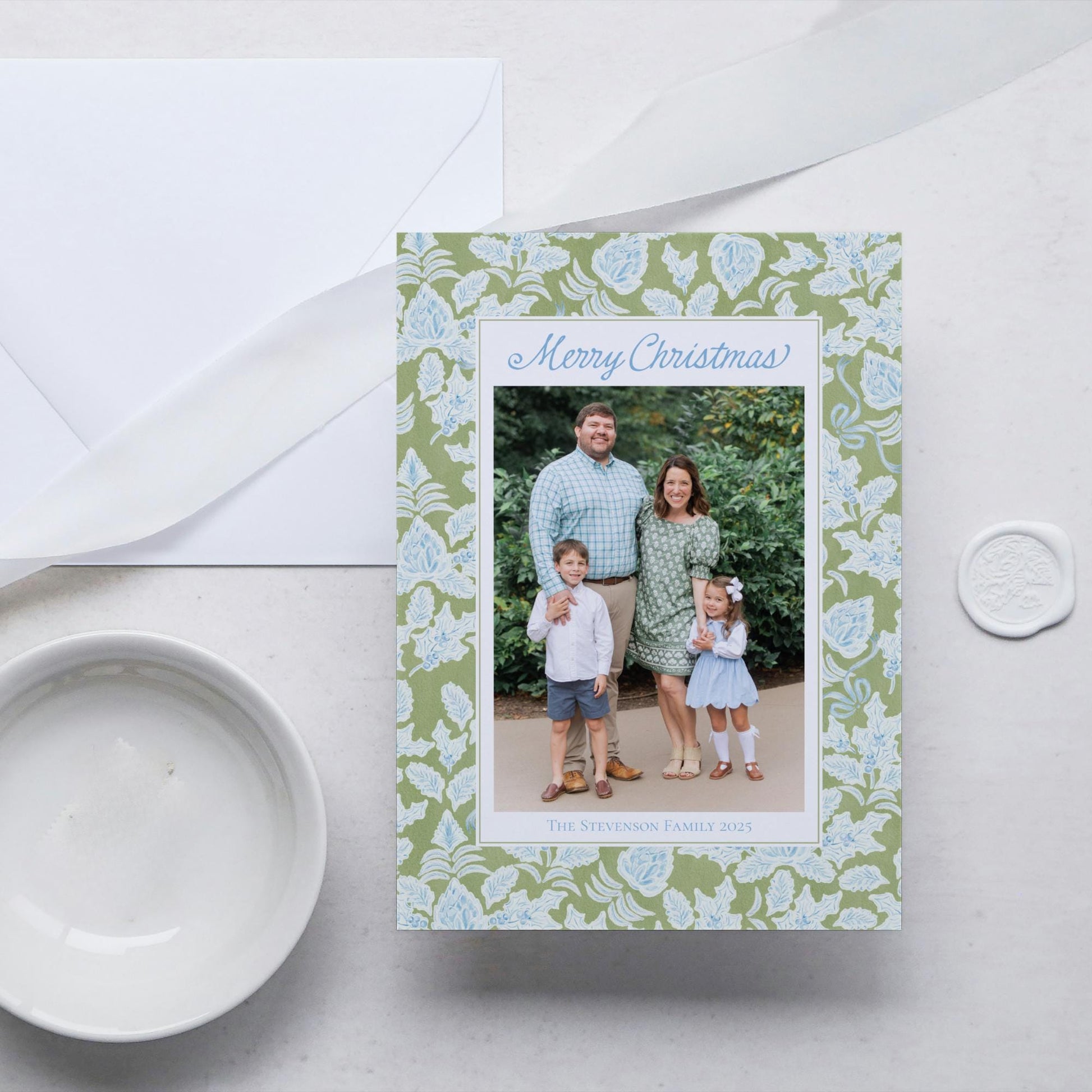 A family photo is displayed on a green and white floral card, with a white envelope and a white wax seal nearby.