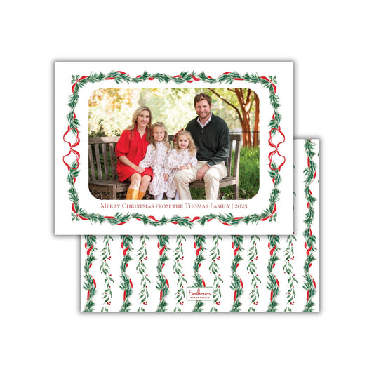 A family portrait of a man, woman, and two young girls, all dressed in festive attire, sitting on a bench in a park setting. The text &quot;Merry Christmas from the Thomas Family (2025)&quot; is displayed around the photo, indicating the holiday season and the family&#39;s wish for a Merry Christmas from their loved ones.