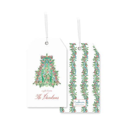 two white tags with Christmas tree designs and text, hanging from strings.