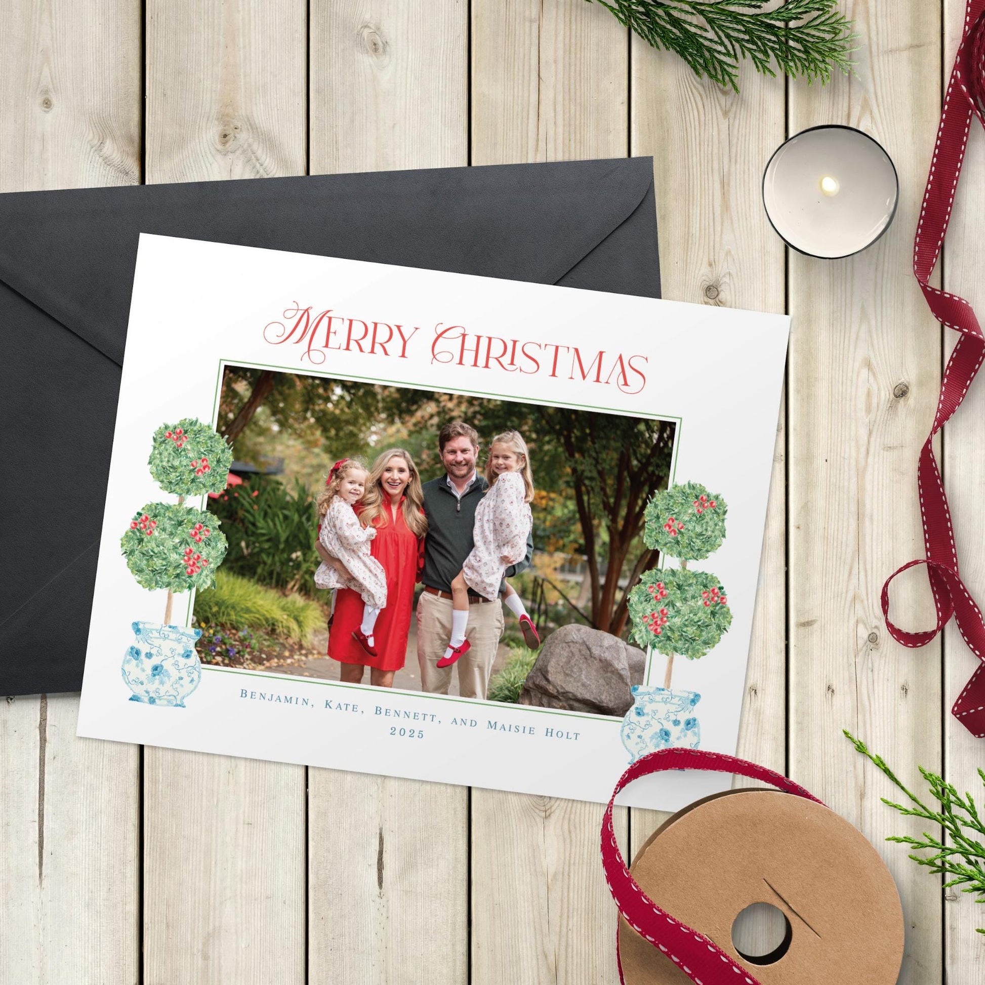 A Christmas card with a photo of a family, along with a ribbon and a candle, placed on a wooden surface.