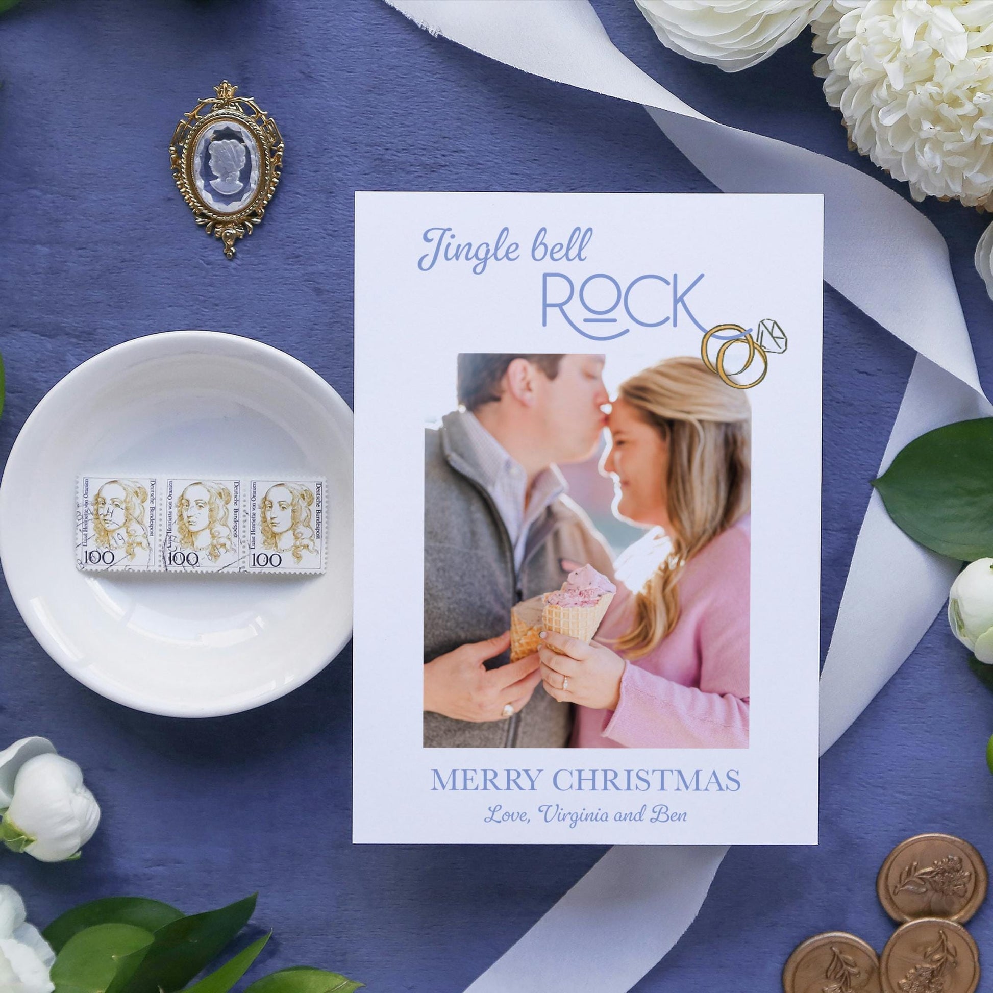 a Christmas card with a photo of a couple kissing, surrounded by various holiday-themed items such as a bowl, flowers, and coins.