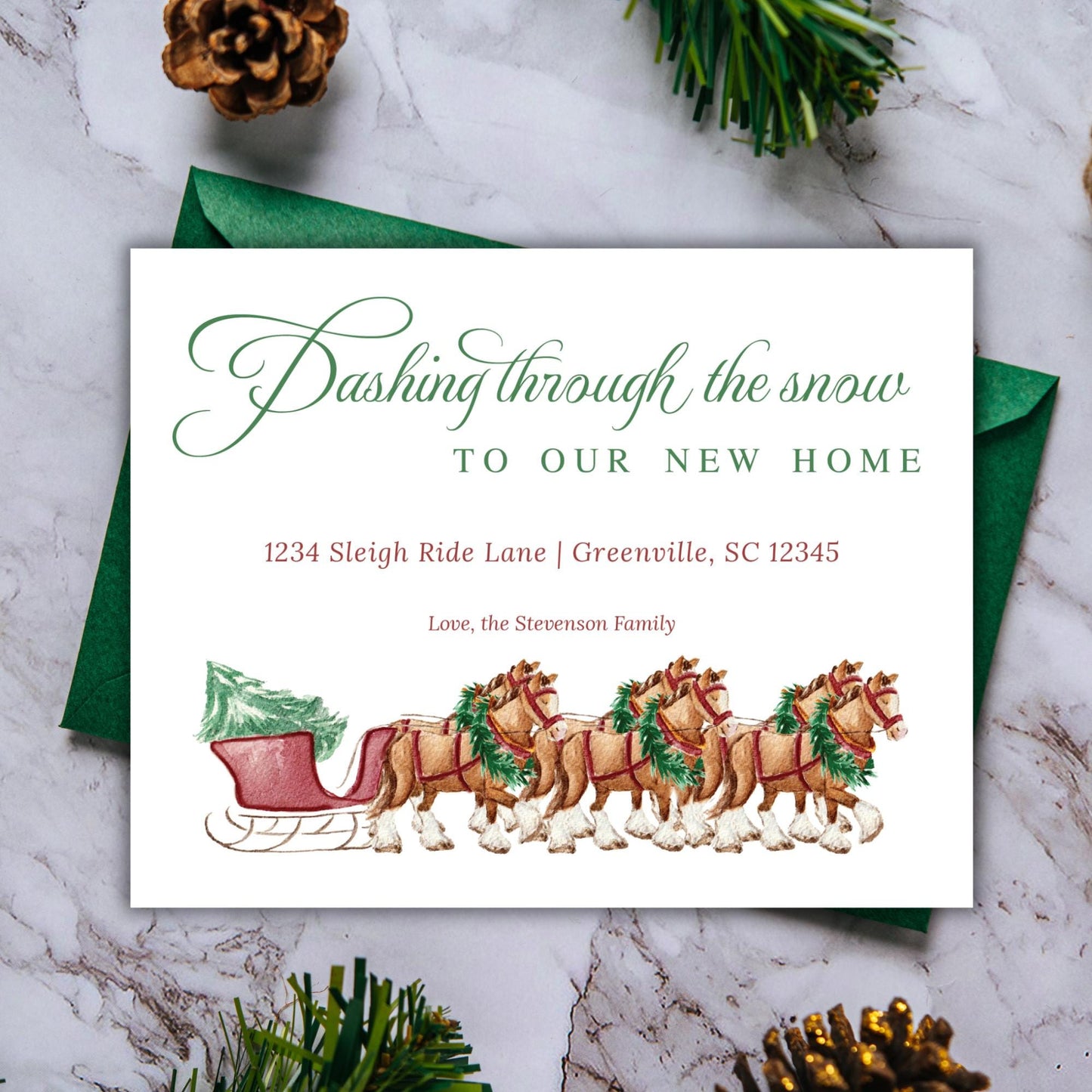 A Christmas-themed greeting card with a sleigh pulled by reindeer, placed on a marble surface with pine cones and a green envelope.