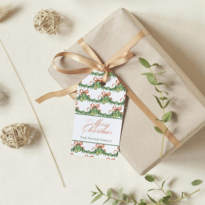 A gift box wrapped in brown paper with a gold ribbon, featuring a Christmas-themed tag that reads "Merry Christmas THE PAYNE FAMILY".