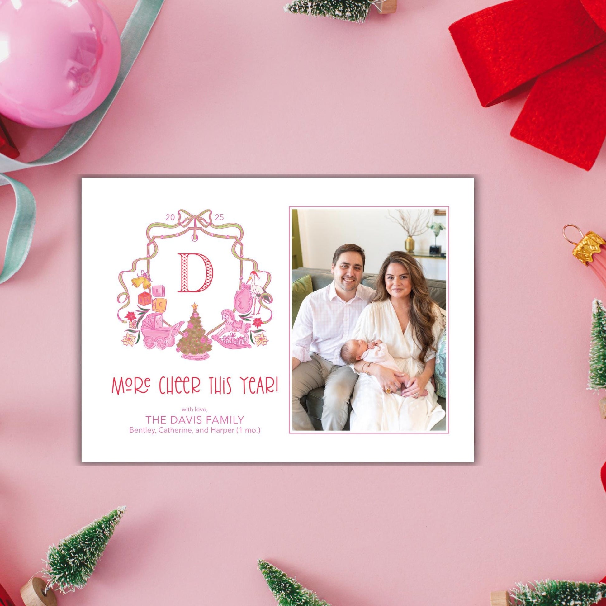 A personalized Christmas card featuring a family photo of a man, woman, and baby, along with decorative elements such as a pink ribbon, a bow, and small Christmas trees.