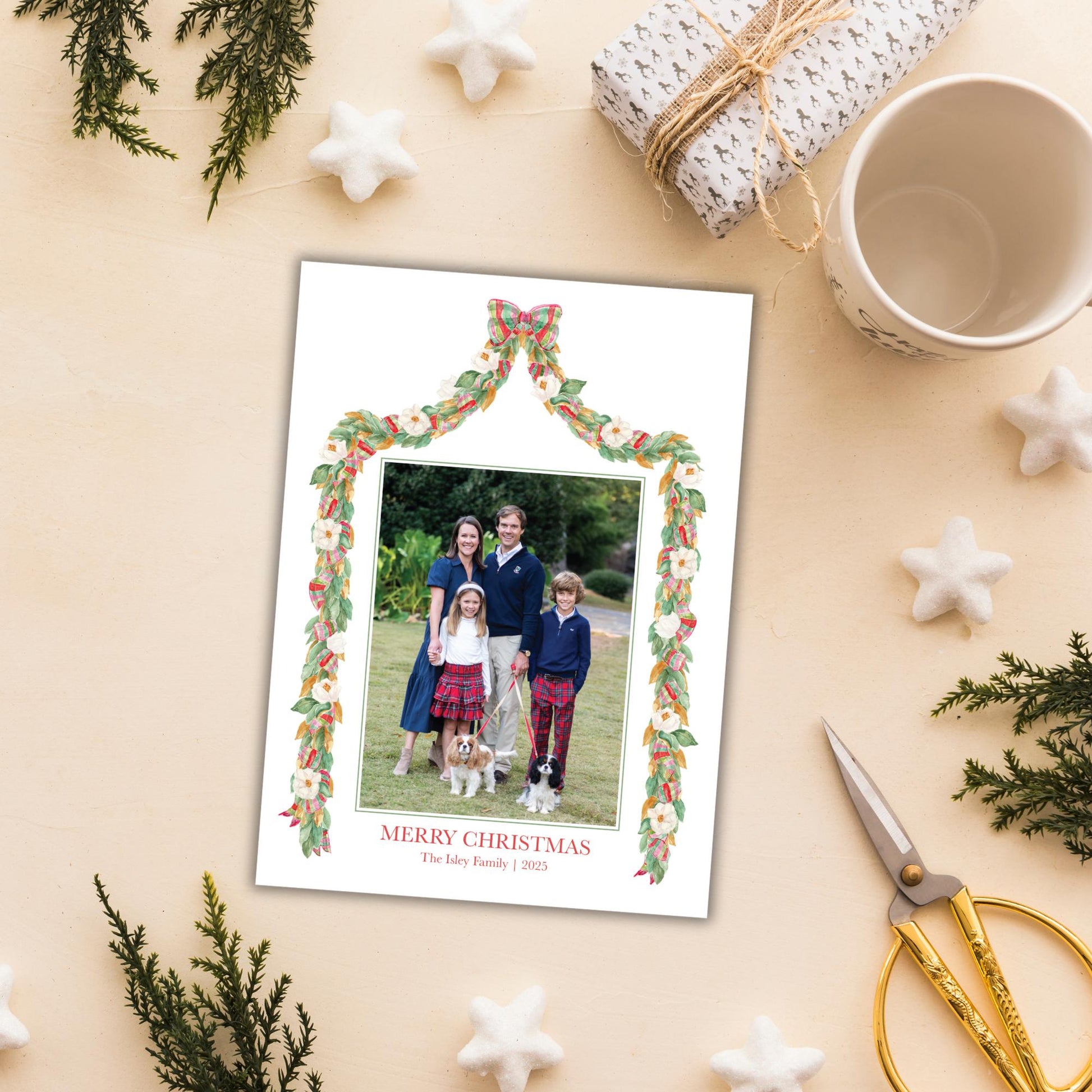 A family portrait of a family of four, with a Christmas-themed frame, is displayed on a table surrounded by holiday decorations, a gift box, and a cup.