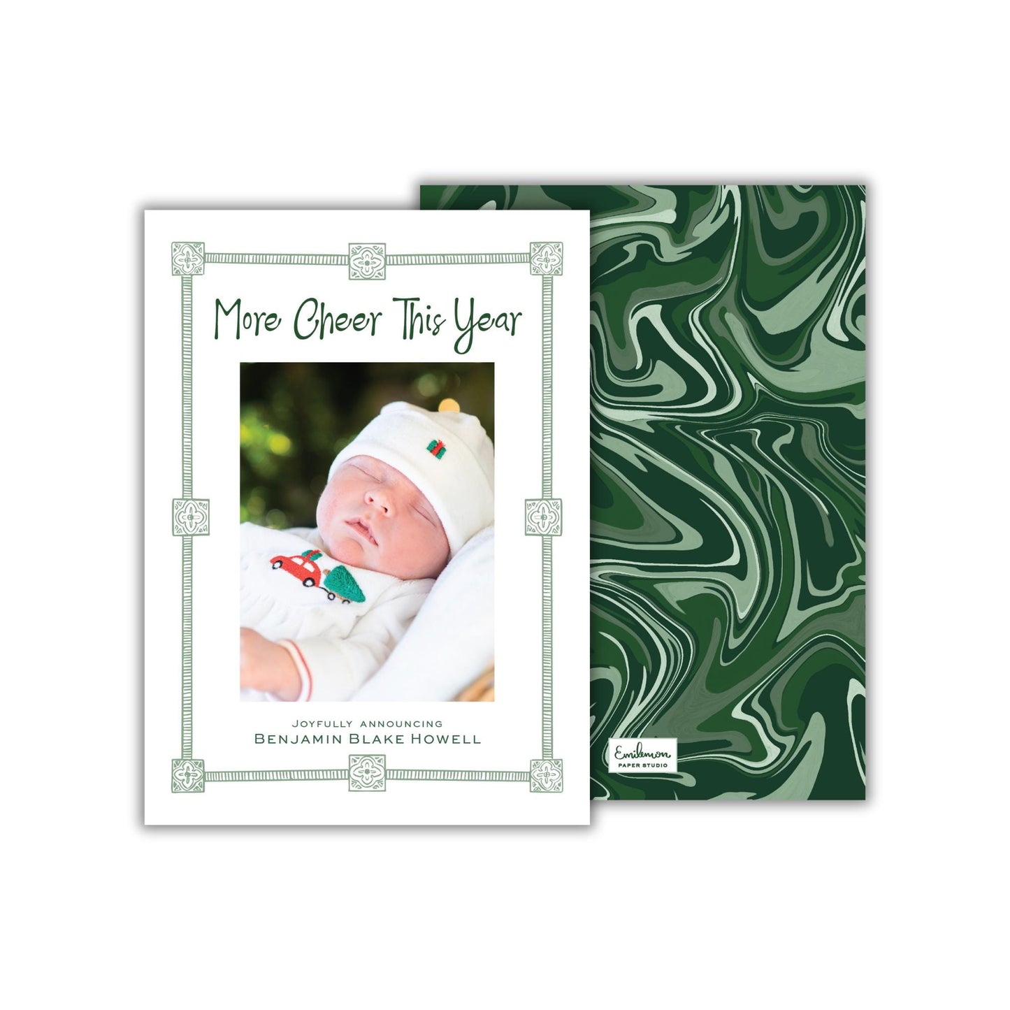 The image is a white card with a photo of a baby wearing a white outfit and a red hat, surrounded by a green border. The card has a green marble-like background.