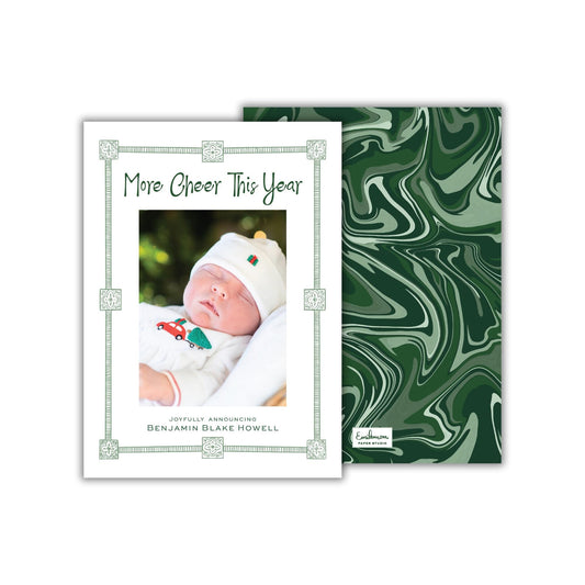 The image is a white card with a photo of a baby wearing a white outfit and a red hat, surrounded by a green border. The card has a green marble-like background.