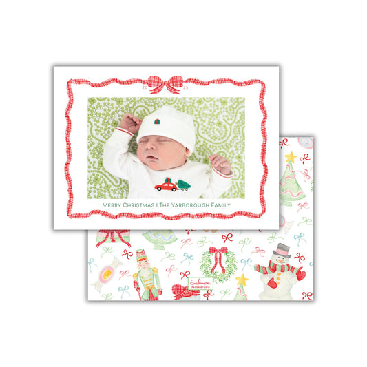 A baby wearing a white outfit and hat is sleeping in a festive Christmas-themed card with a red and white border and a bow.