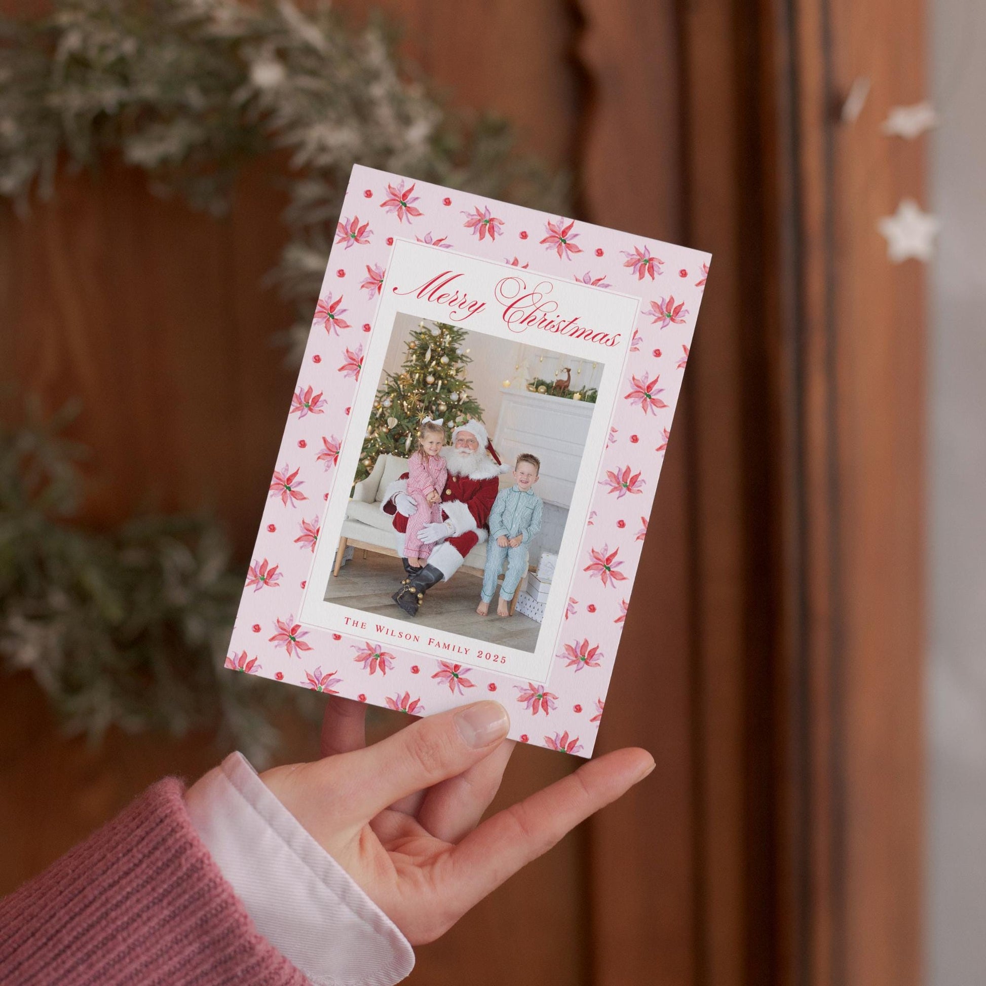 A hand holding a Christmas card with a photo of two children and a Santa Claus figure.