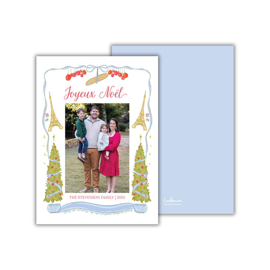 A family portrait of a man, woman, and child, with Christmas trees and the Eiffel Tower in the background, framed by a decorative border.