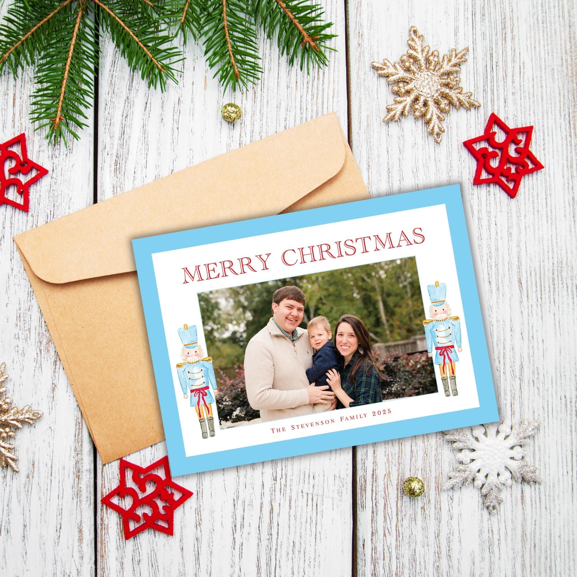 A Christmas card with a family photo and the text &quot;Merry Christmas&quot; is placed on a wooden surface, surrounded by Christmas decorations such as pine branches, star ornaments, and snowflakes.