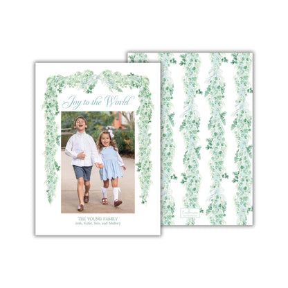 The image is a greeting card featuring two children, a boy and a girl, walking together in a garden setting. The card has a floral border and the text "Joy to the World" written on it.