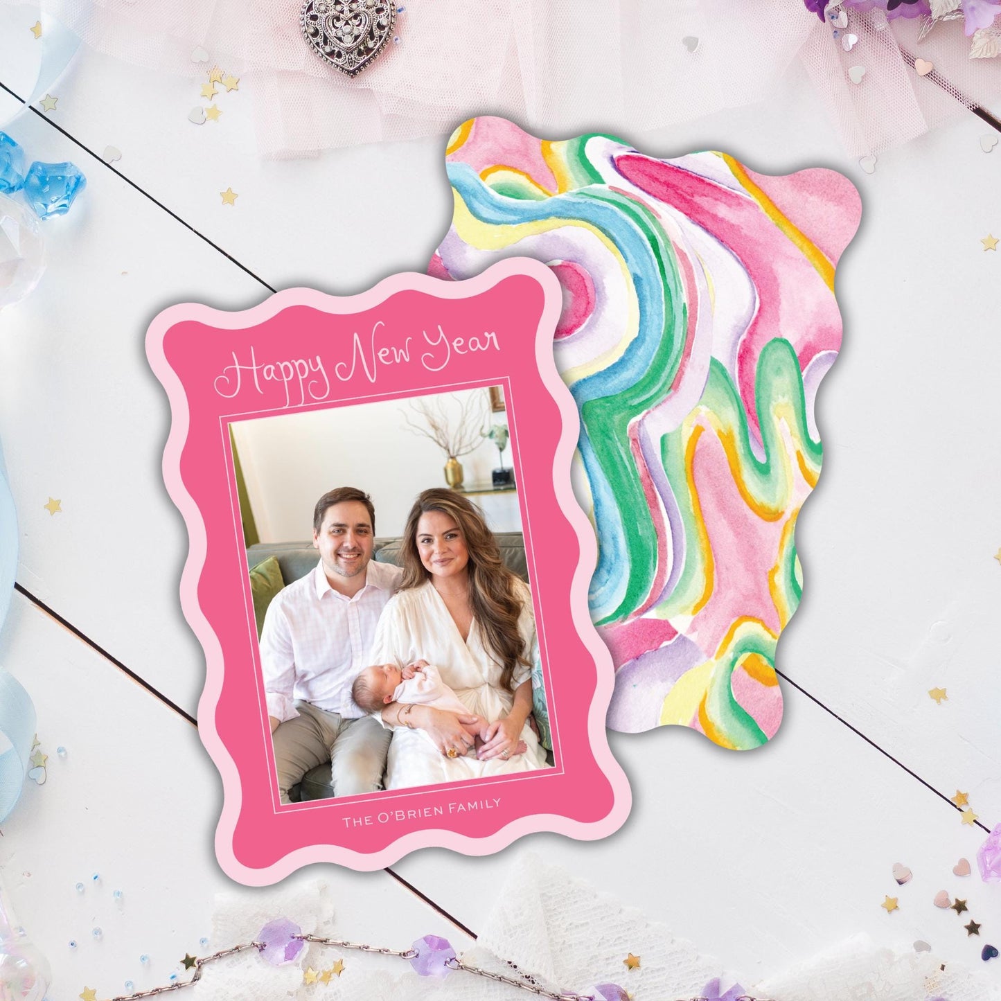 A pink frame with a photo of a couple and a colorful abstract background is placed on a white surface with scattered confetti.