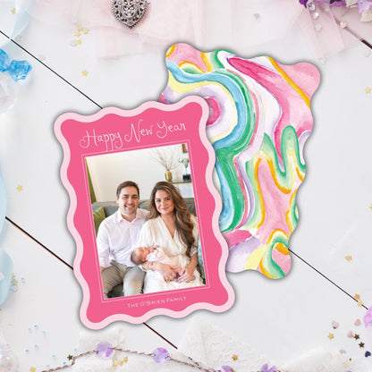 A pink frame with a photo of a couple and a colorful abstract background is placed on a white surface with scattered confetti.