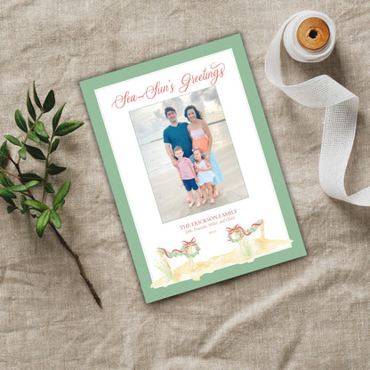 a green and white greeting card with a family photo on it, placed on a beige cloth. There is also a spool of ribbon and a small plant nearby.