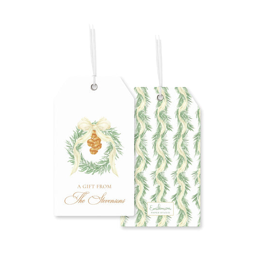 two white tags with holiday-themed designs. The tag on the left has a wreath and a pine cone, and the tag on the right has a repeating pattern of green leaves.