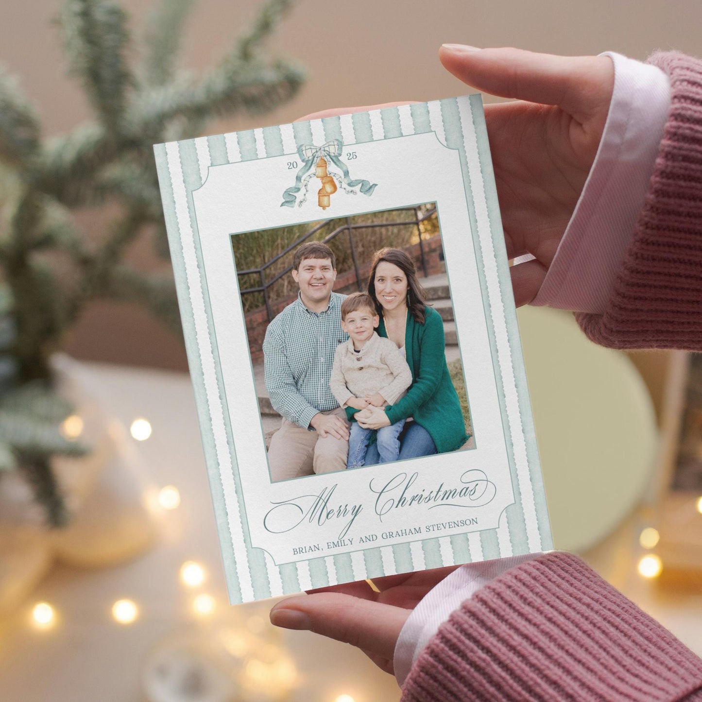 A person is holding a Christmas card with a family photo of a man, woman, and child.