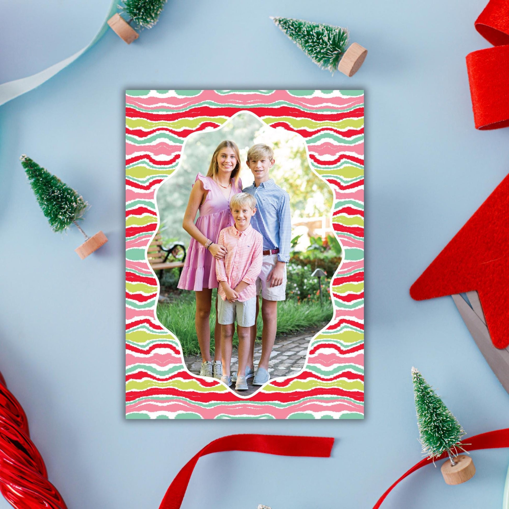 A family portrait of two adults and two children is displayed in a colorful frame, surrounded by Christmas decorations such as small trees and ribbons.