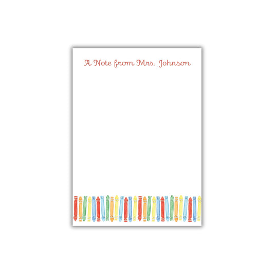 A blank white note card with a border of colored pencils arranged in a row.
