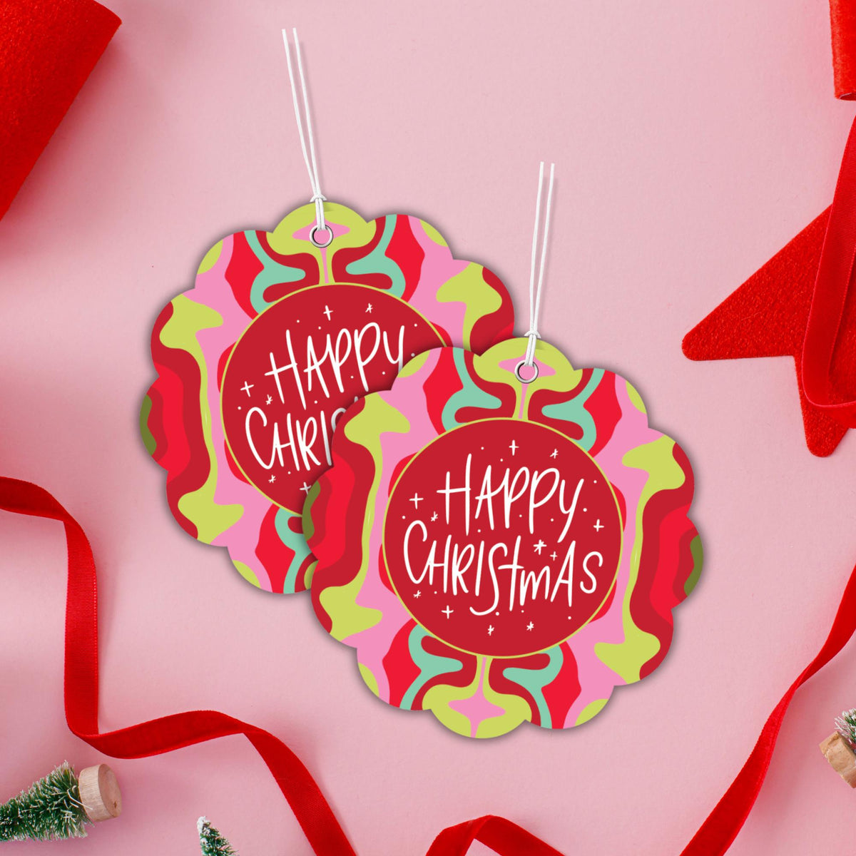 two colorful, flower-shaped Christmas gift tags with the text "Happy Christmas" written on them, hanging from strings against a pink background.