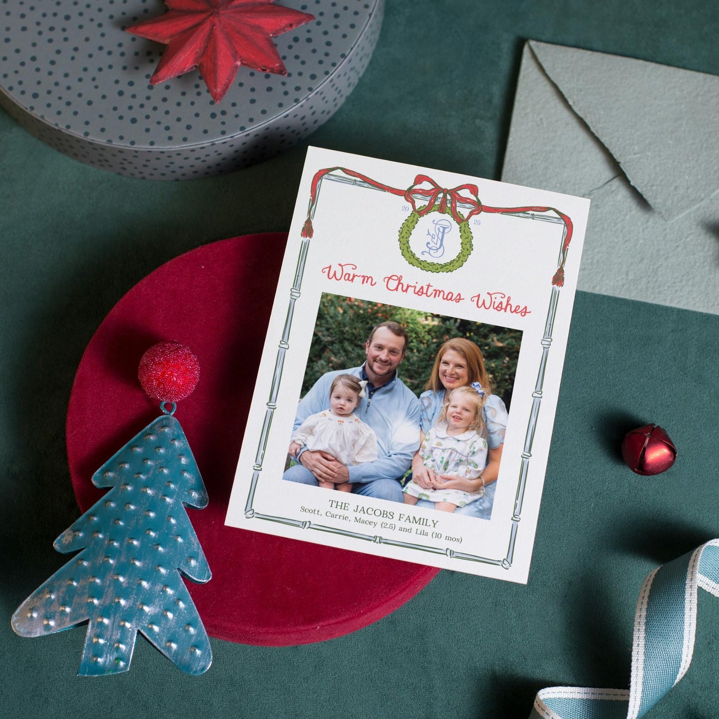 a Christmas card with a family photo, a red bow, and other holiday decorations on a green tablecloth.