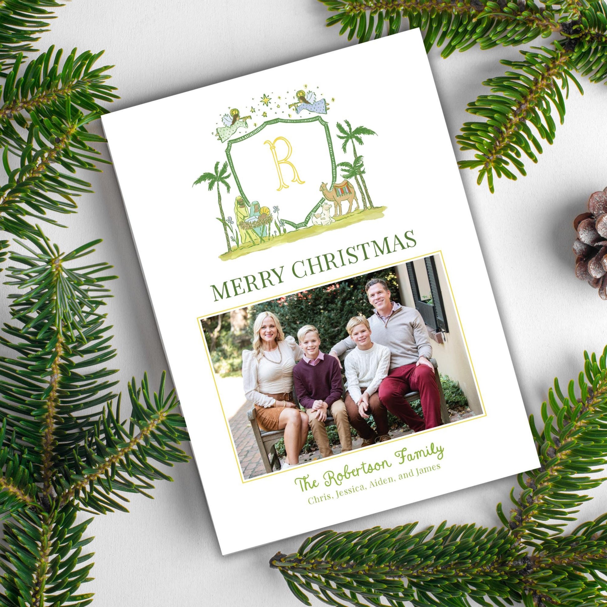 A white card with a family photo and a crest design, surrounded by pine branches and pine cones, indicating a holiday or seasonal setting.
