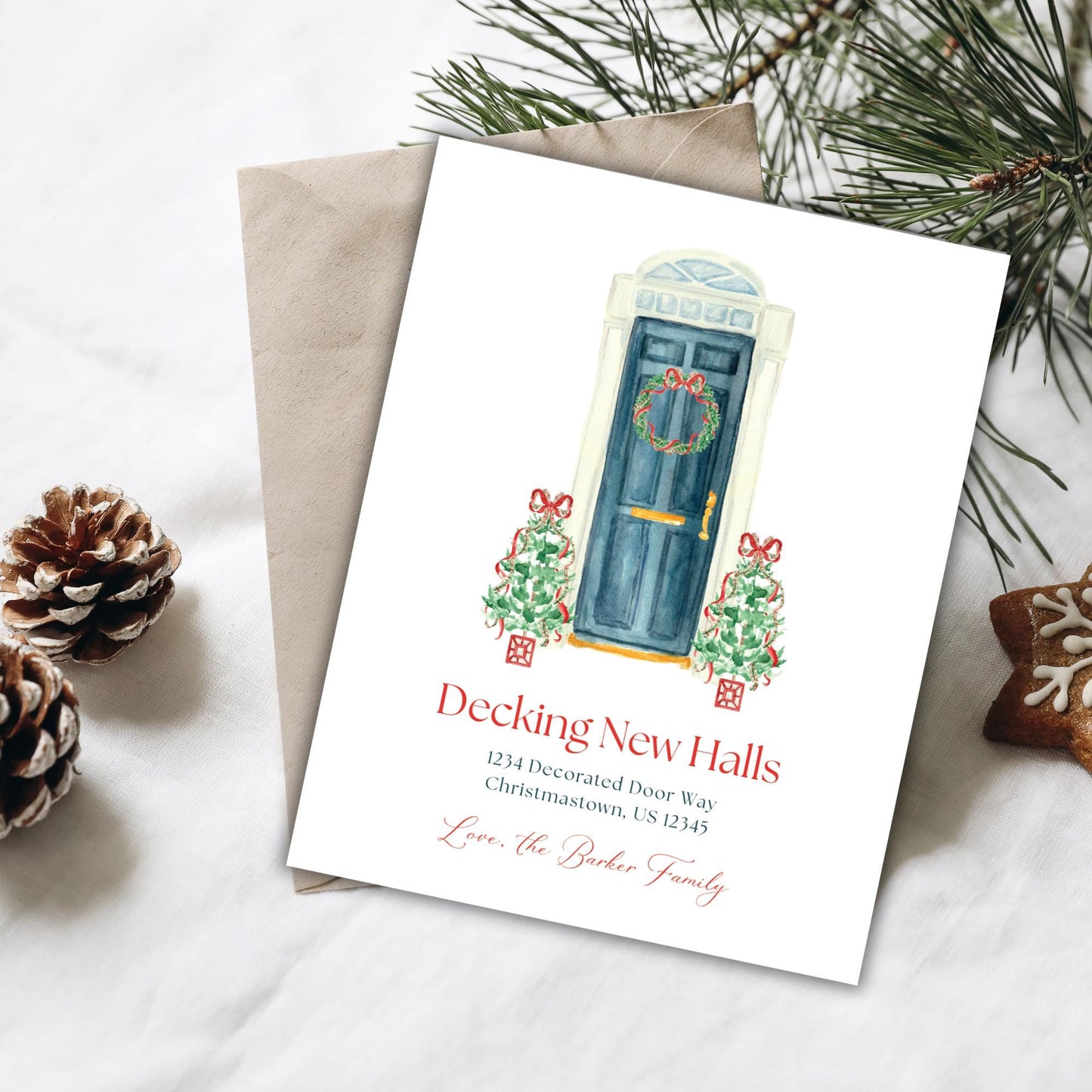 A white card with a festive illustration of a decorated door and wreath, surrounded by pine branches and pine cones, placed on a white surface.
