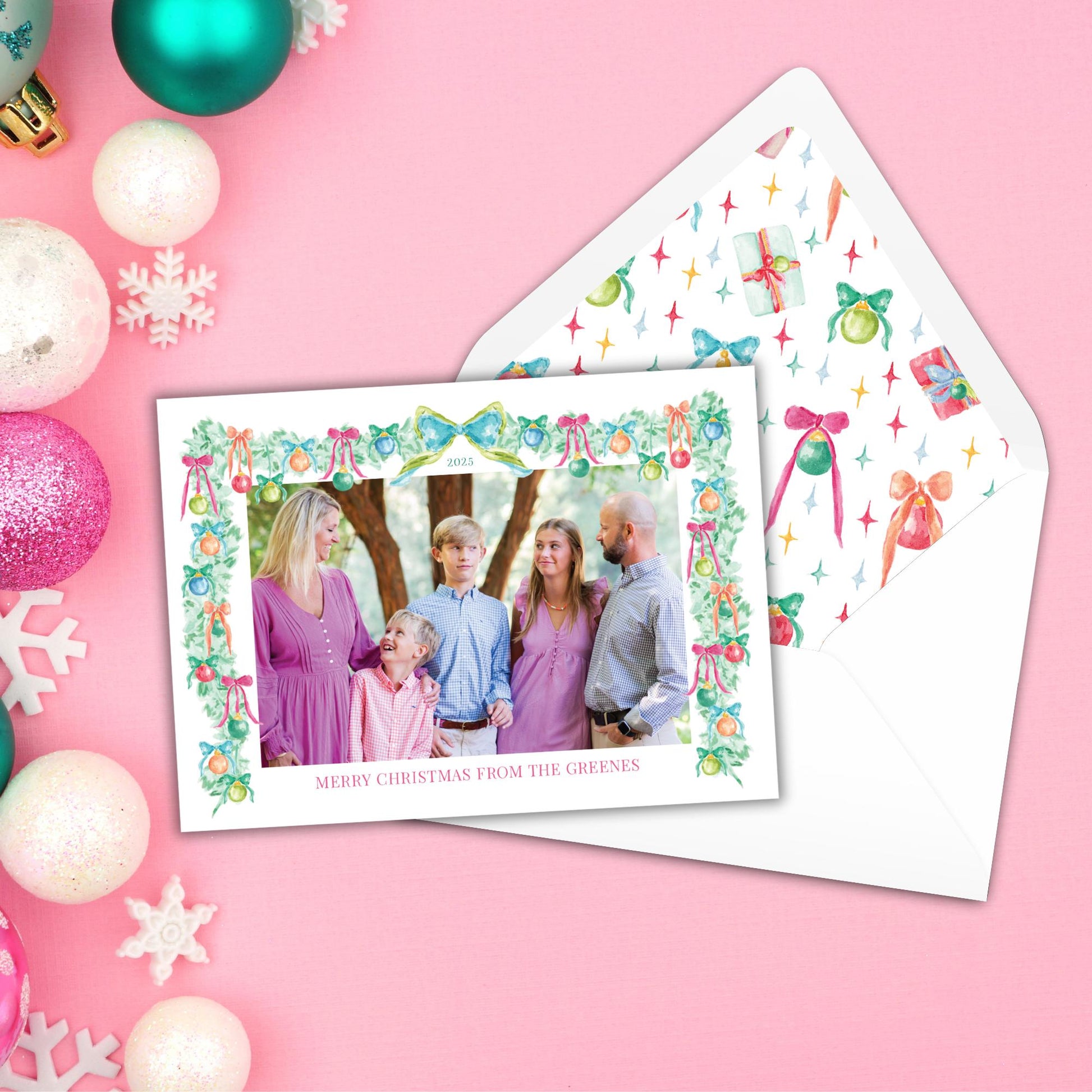 A Christmas card with a family photo of a group of people, surrounded by Christmas ornaments and a pink background.