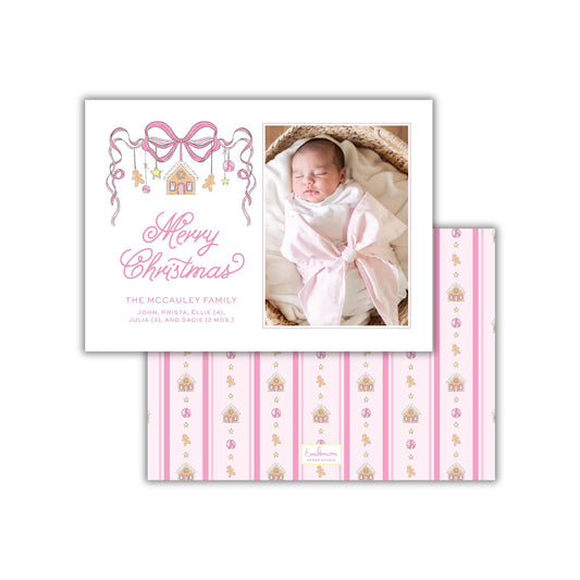 A white card with a photo of a baby swaddled in a pink blanket, along with a decorative bow and the text "Merry Christmas" and "The McCauley Family" written on it.